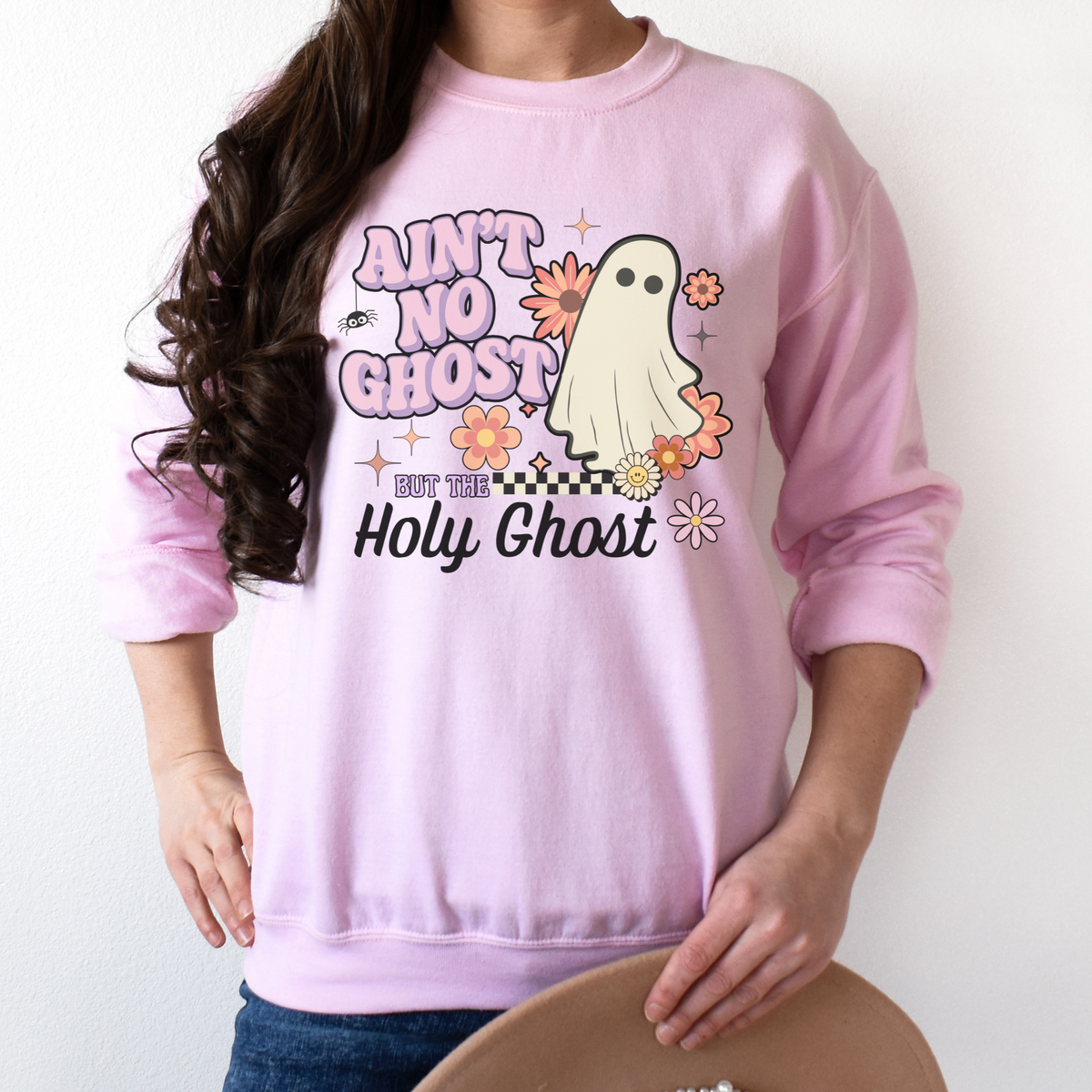Person wearing a pink sweatshirt with a ghost graphic and text on a plain background