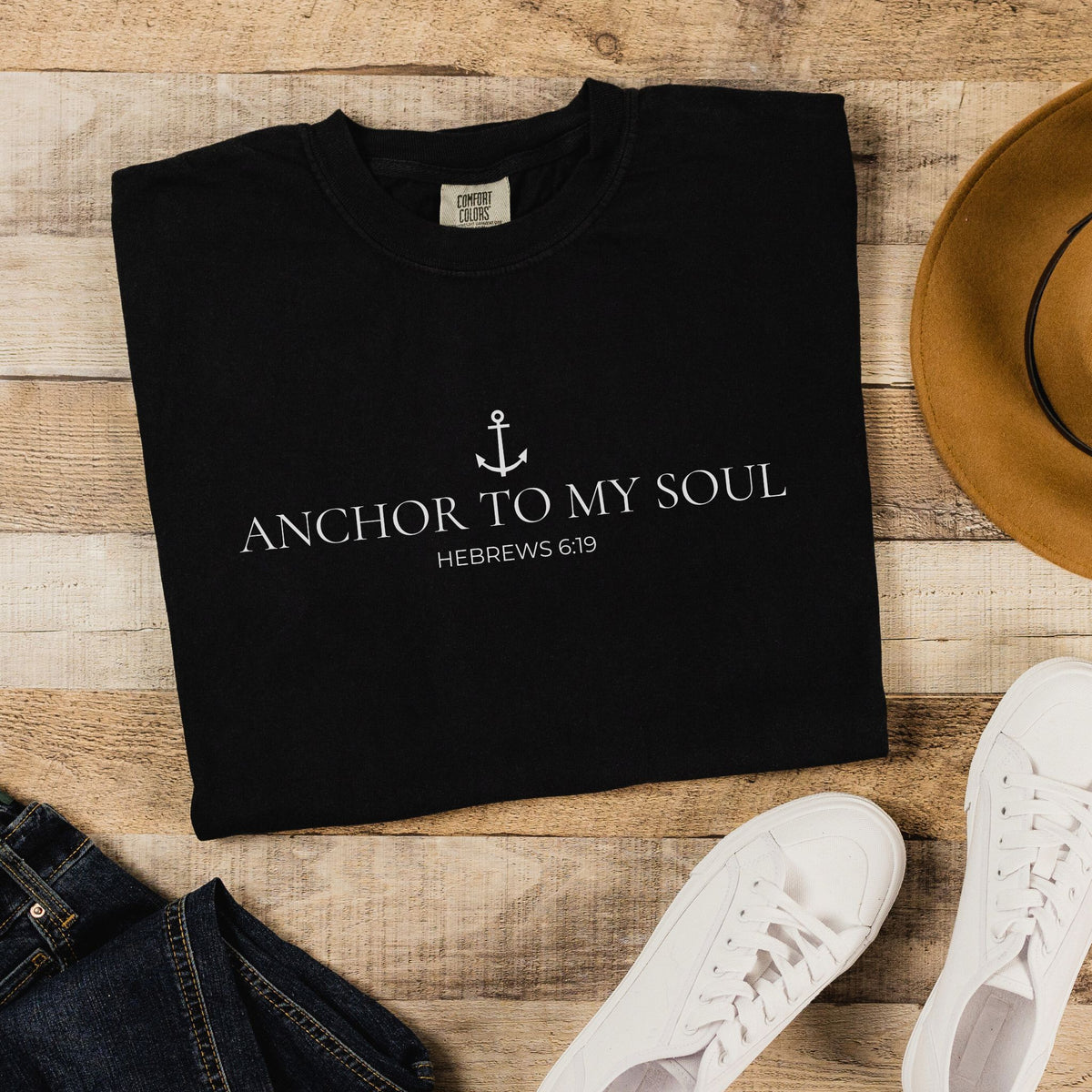 Black t-shirt with 'Anchor to My Soul' text on a wooden surface with shoes and jeans.