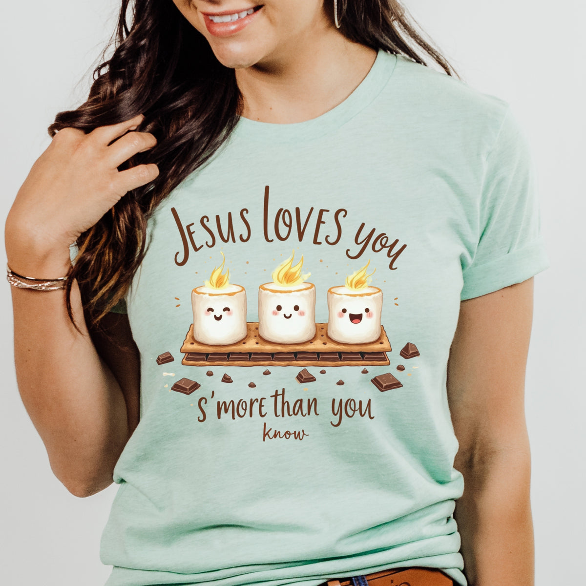 Person wearing a light blue t-shirt with a graphic and text about Jesus loves you 's'more' than you know.