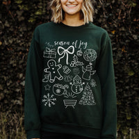 Person wearing a dark green sweatshirt with white Christmas-themed graphics and text 'season of joy' against a natural background.