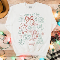 White sweatshirt with Christmas-themed graphics on a wooden surface with lights and plaid fabric.