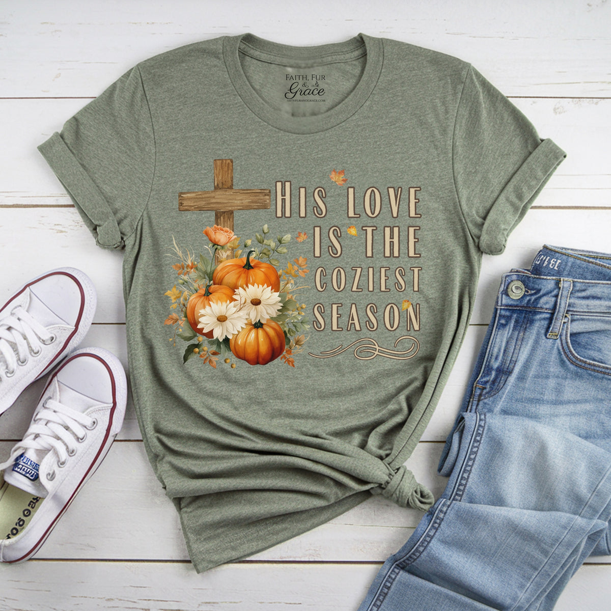 Green t-shirt with pumpkin and cross design on a wooden surface with shoes and jeans.