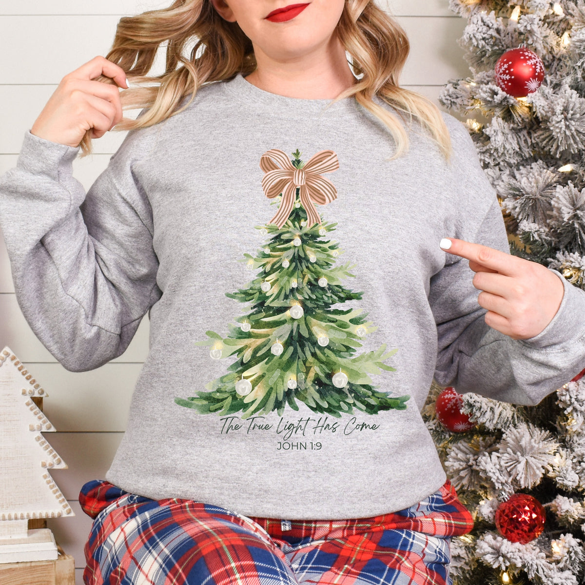 Person wearing a gray sweatshirt with a Christmas tree design in front of a decorated tree.