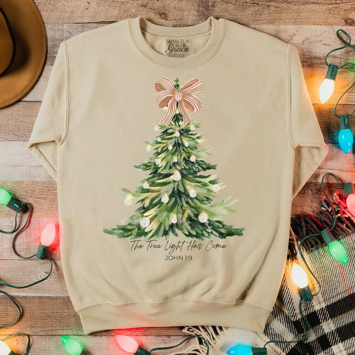 Beige sweatshirt with Christmas tree design and lights on a wooden surface