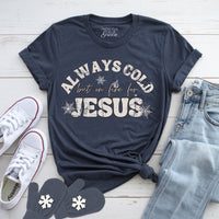 Navy blue t-shirt with 'Always Cold but on Fire for Jesus' text, white sneakers, jeans, and mittens on a light wooden surface.