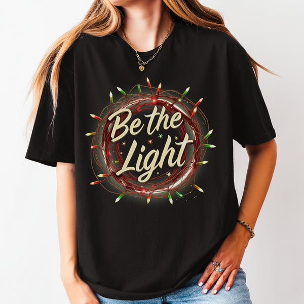 Person wearing a black t-shirt with 'Be the Light' design on a plain background