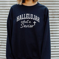 Navy blue sweatshirt with 'HALLELUJAH what a Savior' text and cross symbol on a corrugated metal background