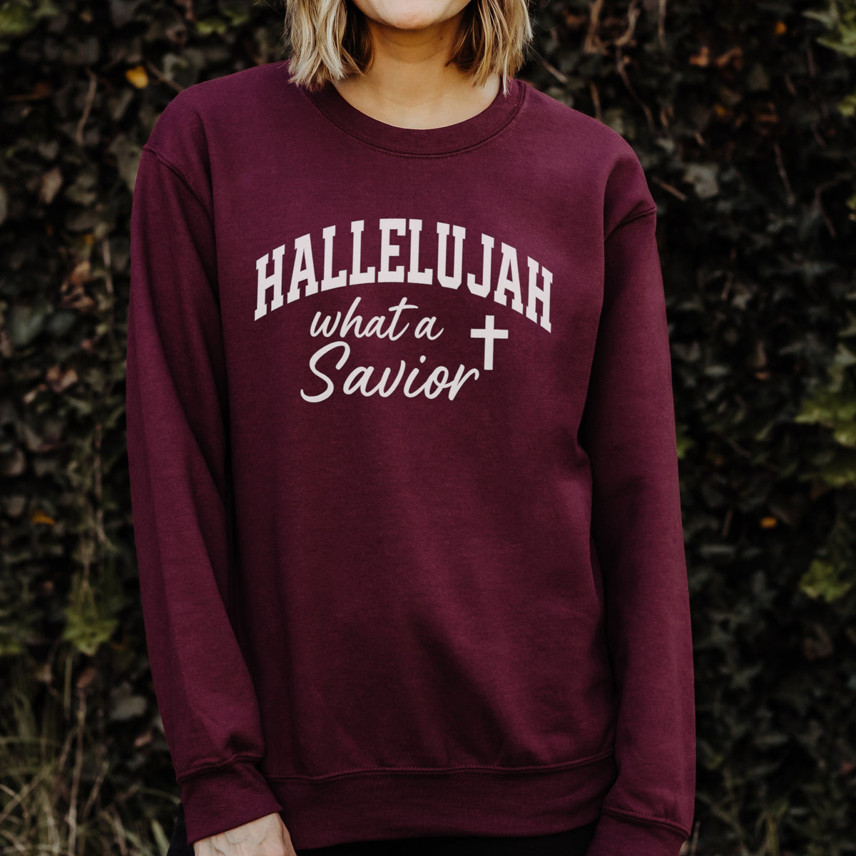 Maroon sweatshirt with 'HALLELUJAH what a Savior' text and cross symbol, worn by a person against a dark background.