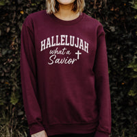 Maroon sweatshirt with 'HALLELUJAH what a Savior' text and cross symbol, worn by a person against a dark background.