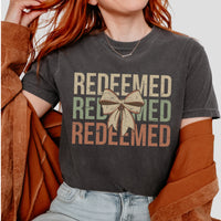 Person wearing a dark gray t-shirt with 'REDEEMED' text and a bow graphic.