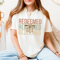 Person wearing a white t-shirt with 'REDEEMED' text and a bow graphic.
