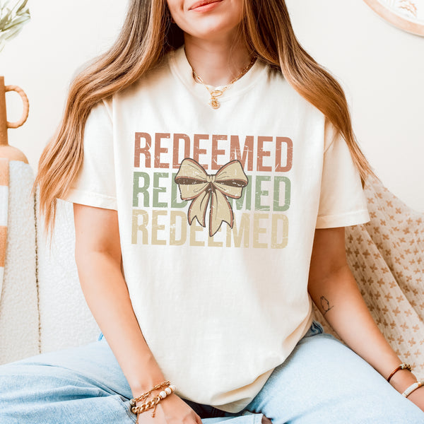 Person wearing a white t-shirt with 'REDEEMED' text and a bow graphic.