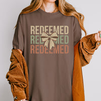 Person wearing a brown shirt with 'REDEEMED' text and a bow graphic.