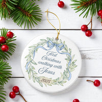 Decorative Christmas ornament with wreath design and text on a white wooden background with pine branches and berries.
