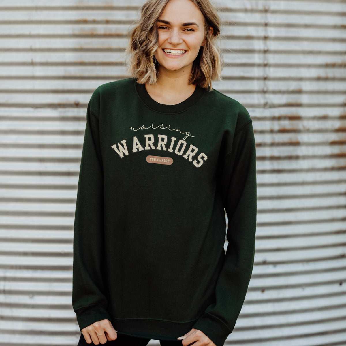 Person wearing a dark green sweatshirt with 'Warriors' printed on it against a corrugated metal background