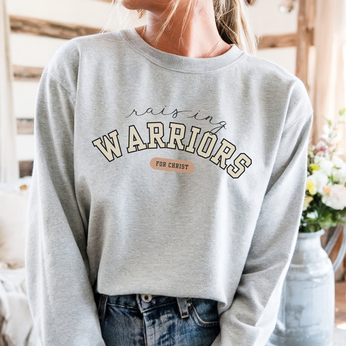 Person wearing a gray sweatshirt with 'Raising Warriors for Christ' text in a casual setting.