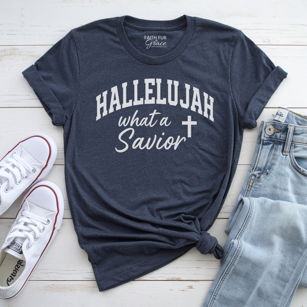 Navy blue t-shirt with 'HALLELUJAH what a Savior' text, white sneakers, and light blue jeans on a wooden surface.
