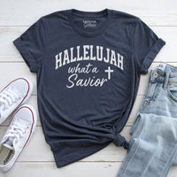 Navy blue t-shirt with 'HALLELUJAH what a Savior' text, white sneakers, and light blue jeans on a wooden surface.