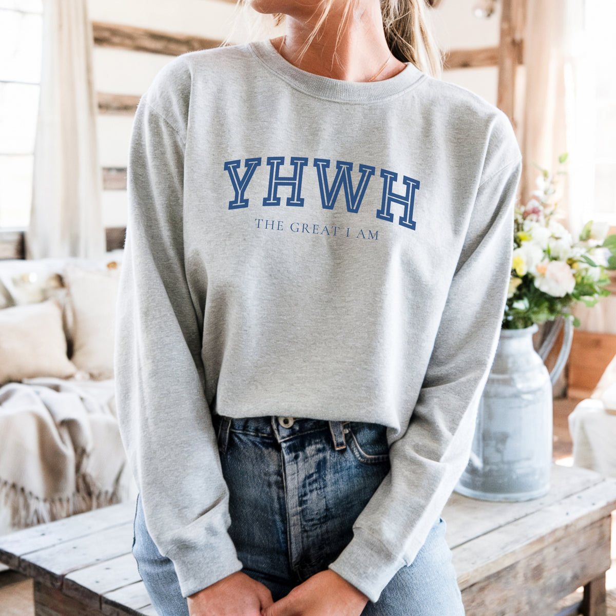 Person wearing a gray sweatshirt with 'YHWH THE GREAT I AM' text in a casual setting.