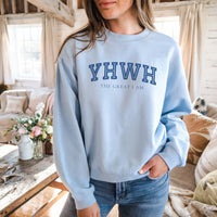 Person wearing a light blue sweatshirt with 'YHWH THE GREAT I AM' text in a cozy indoor setting.