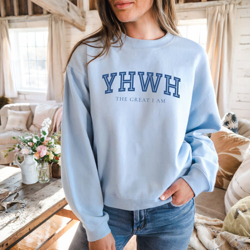Person wearing a light blue sweatshirt with 'YHWH THE GREAT I AM' text in a cozy indoor setting.