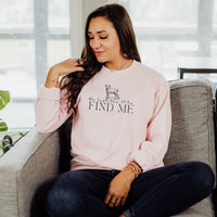 Woman wearing a pink sweatshirt with text and a graphic, sitting on a couch.