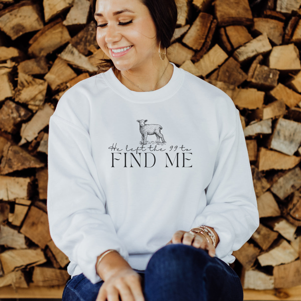 Woman wearing a white sweatshirt with text and a graphic, sitting in front of stacked wood.