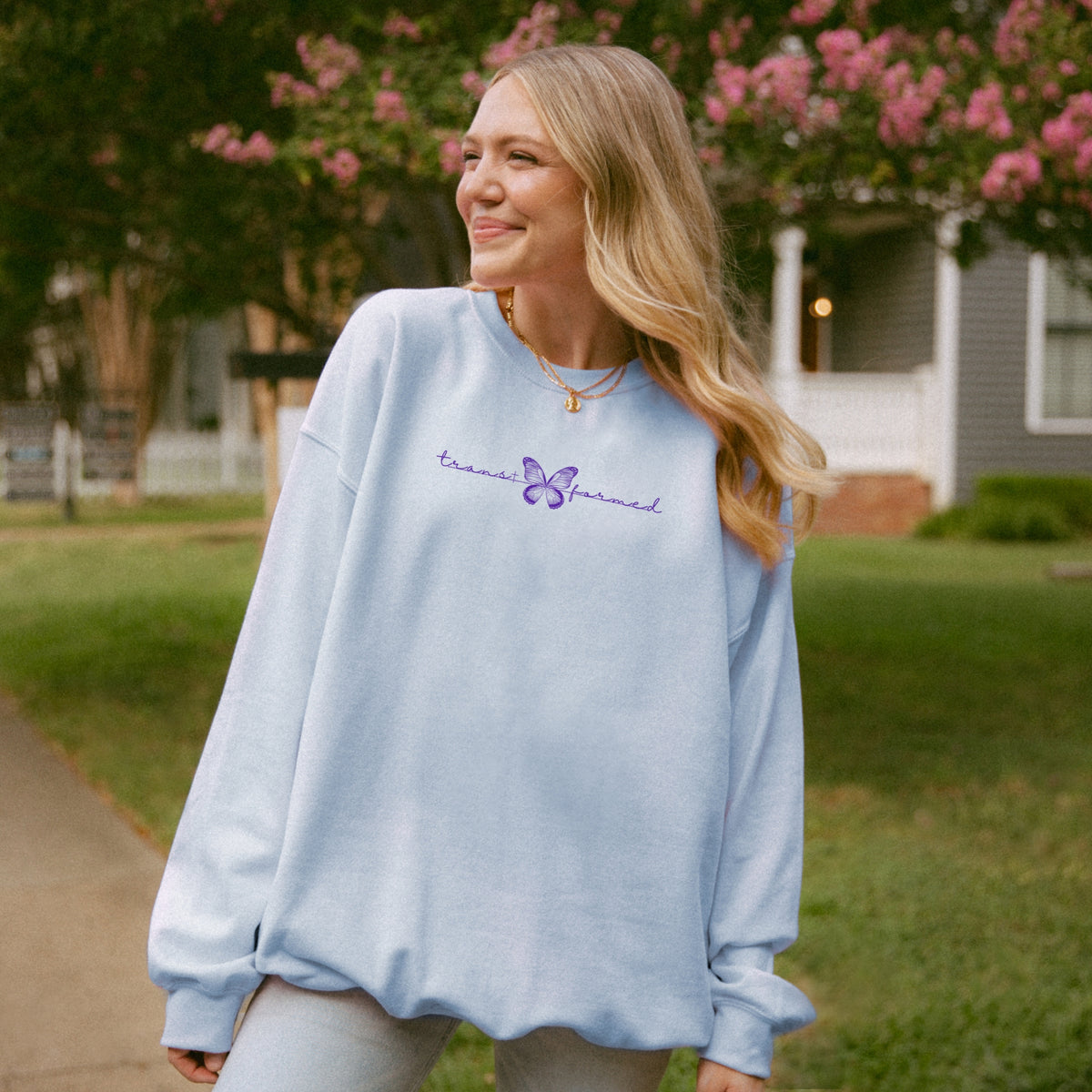 Woman wearing a light blue sweatshirt with text and a butterfly design outdoors.