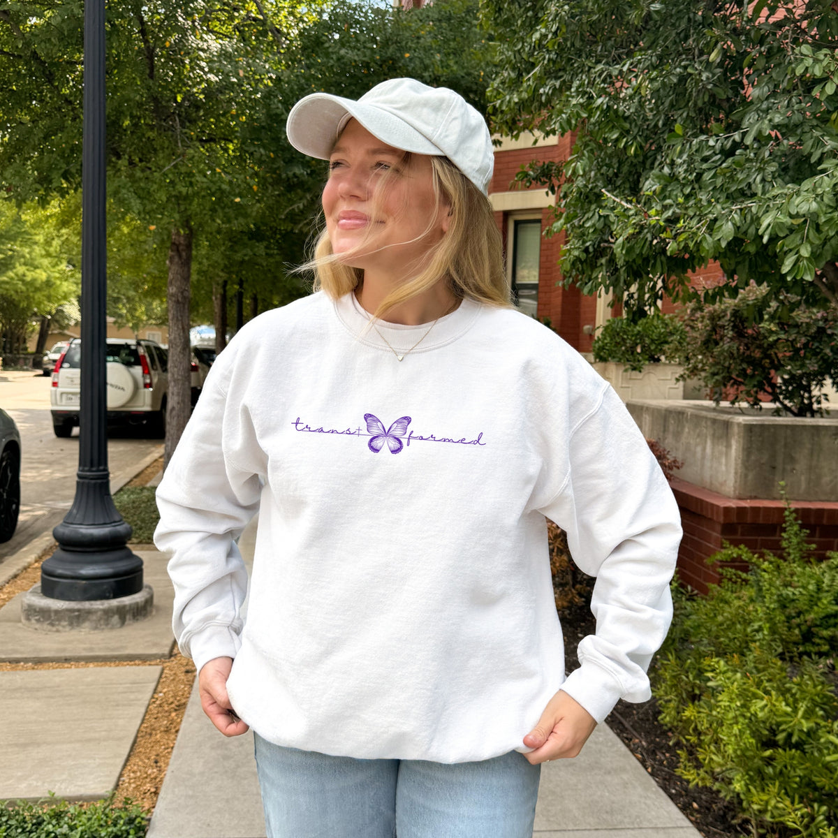 Person wearing a white sweatshirt with a butterfly and text, standing outdoors.