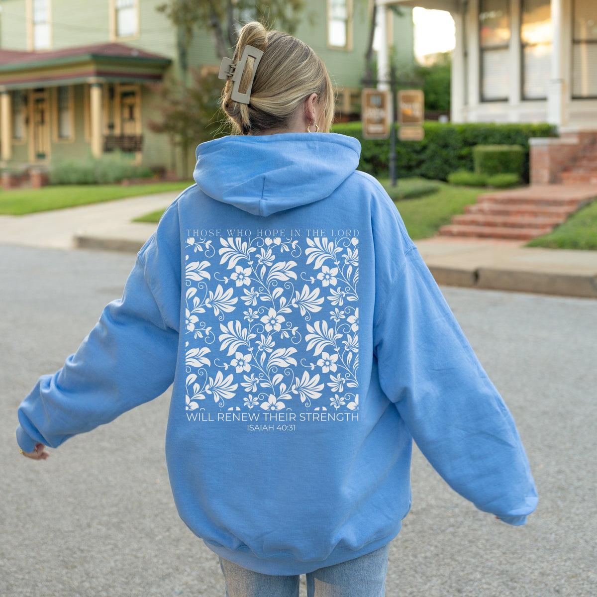 Person wearing a blue hoodie with floral design and text on the back, standing in a residential area.