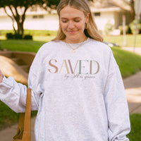 Woman wearing a gray sweatshirt with 'SAVED by His grace' text outdoors.