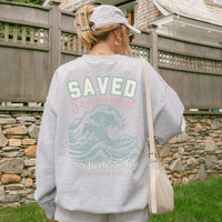 Person wearing a gray sweatshirt with a design and text on the back, standing outdoors.