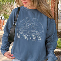 Person wearing a blue sweatshirt with 'Living Water' text and design outdoors.