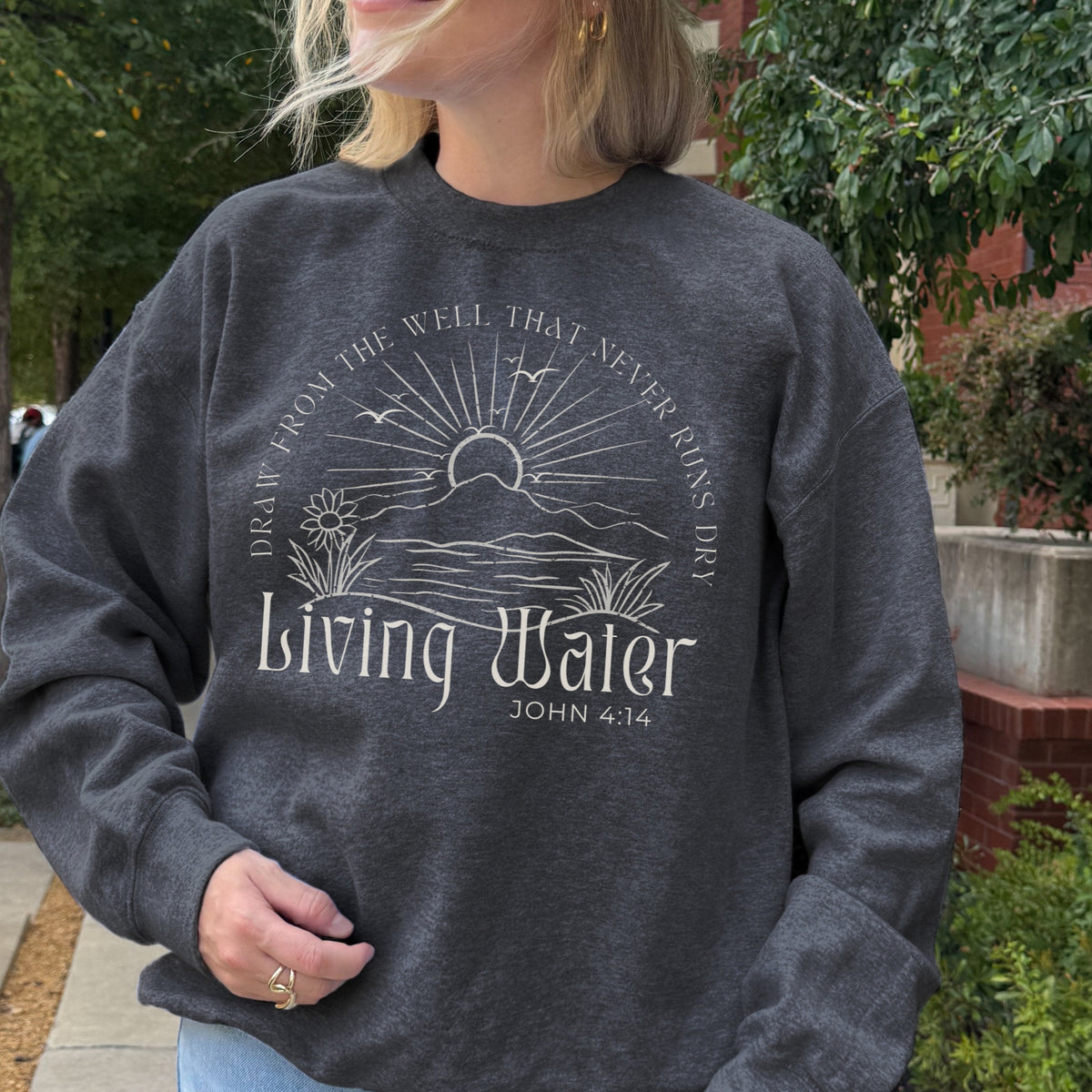 Person wearing a dark gray sweatshirt with 'Living Water' design and text outdoors.
