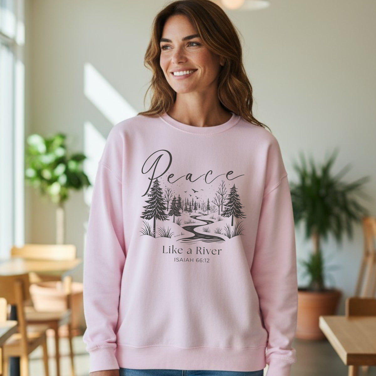 Woman wearing a pink sweatshirt with a nature-themed design and text in a casual indoor setting.