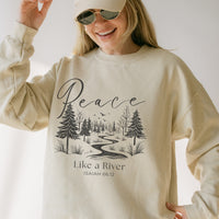 Person wearing a beige sweatshirt with a nature-themed design and 'Peace Like a River' text.