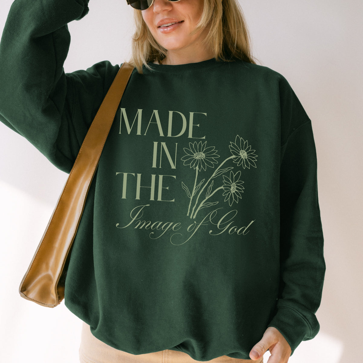 Person wearing a green sweatshirt with text and floral design, holding a brown bag.