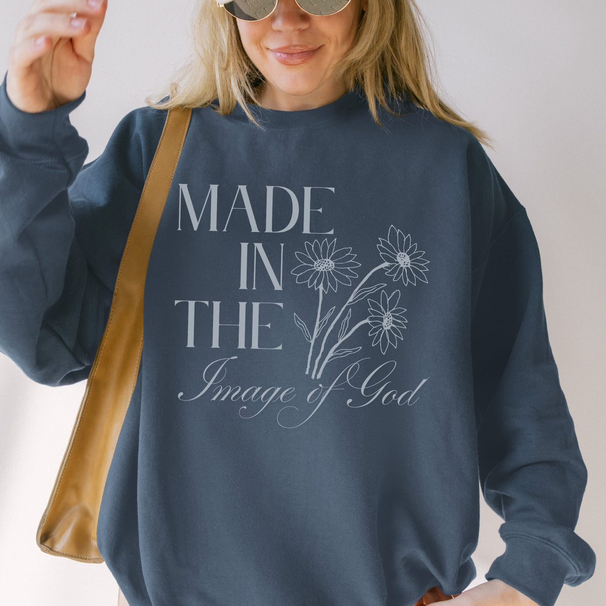 Person wearing a navy sweatshirt with 'Made in the Image of God' text and floral design.
