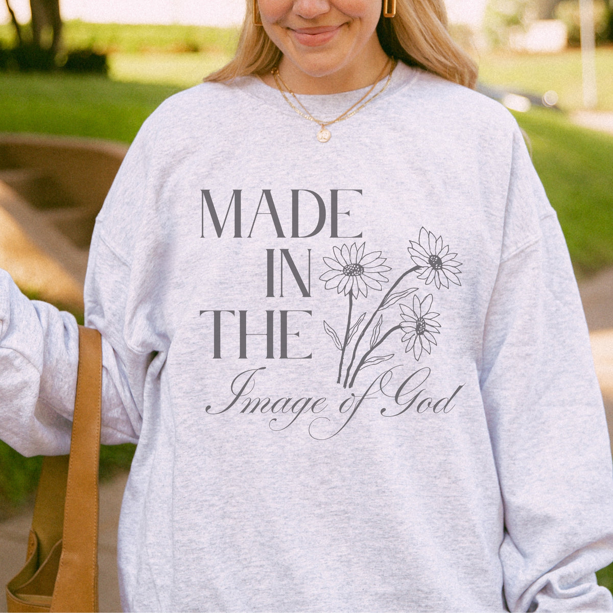 Person wearing a gray sweatshirt with 'Made in the Image of God' text and floral design outdoors.