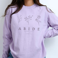 Person wearing a lavender long-sleeve shirt with floral designs and text.