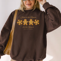 Person wearing a brown sweatshirt with Christmas-themed text and graphics.
