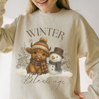 Beige sweatshirt with a winter-themed design featuring a cow and snowman, text 'Winter Blessings'.
