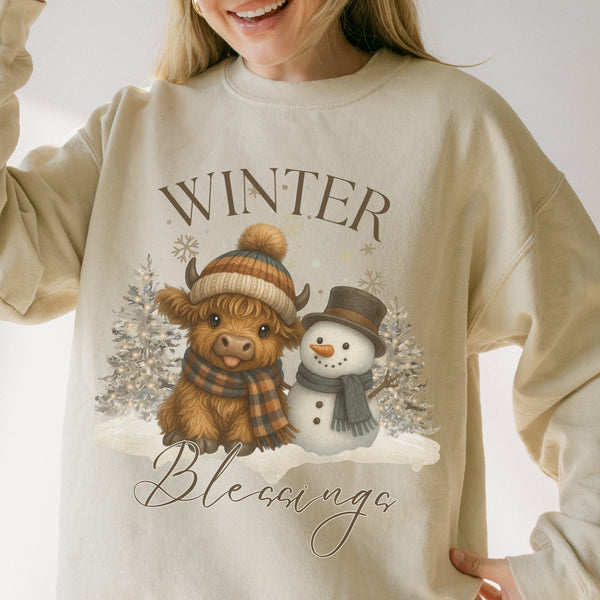 Beige sweatshirt with a winter-themed design featuring a cow and snowman, text 'Winter Blessings'.