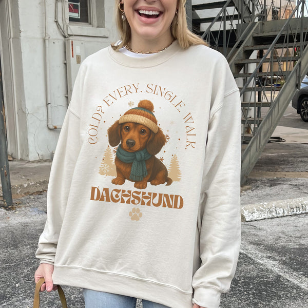 Person wearing a beige sweatshirt with a dachshund graphic and text outdoors.