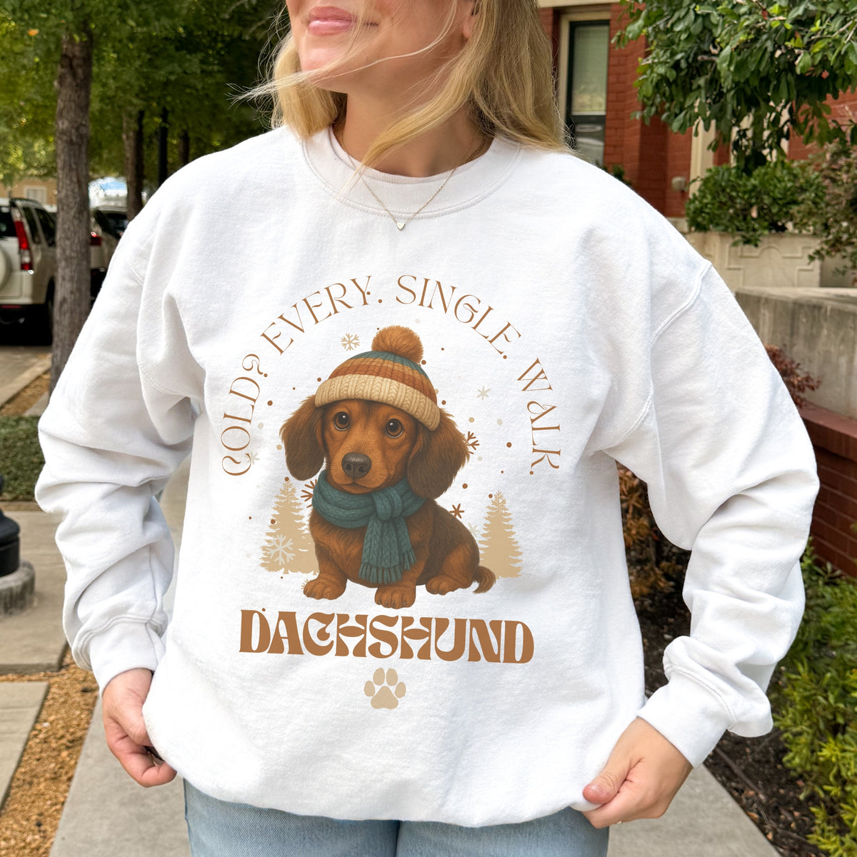 Person wearing a white sweatshirt with a dachshund graphic and text outdoors.