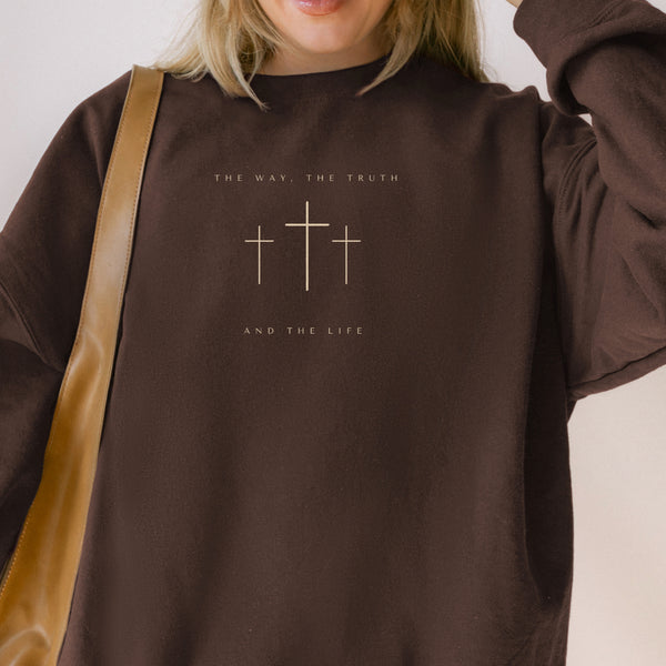 Brown sweatshirt with cross design and text worn by a person, against a neutral background