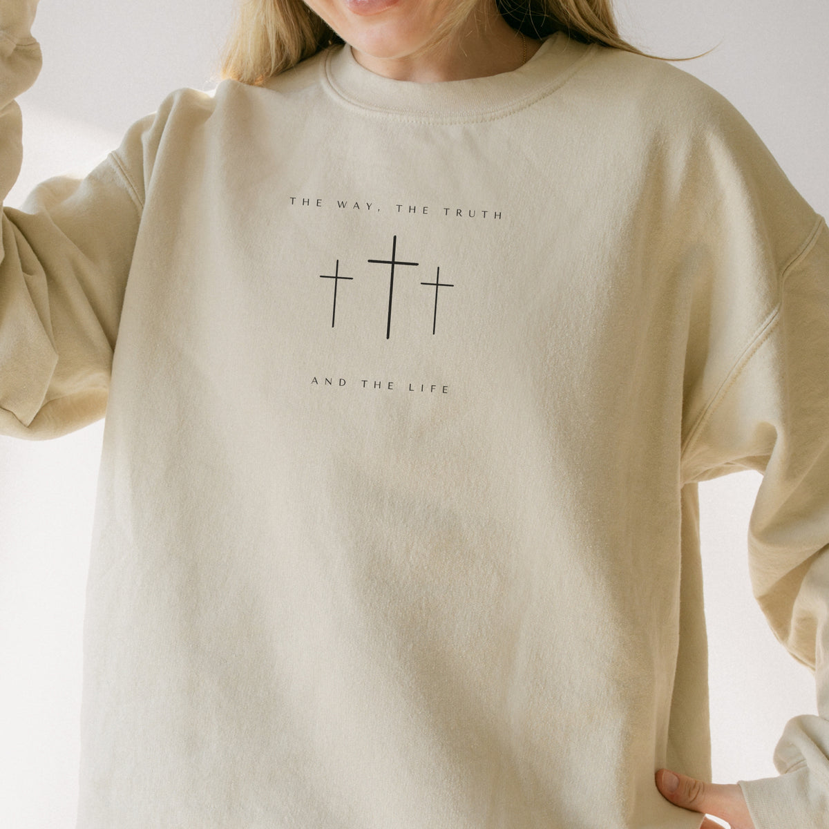 Beige sweatshirt with cross design and text worn by a person