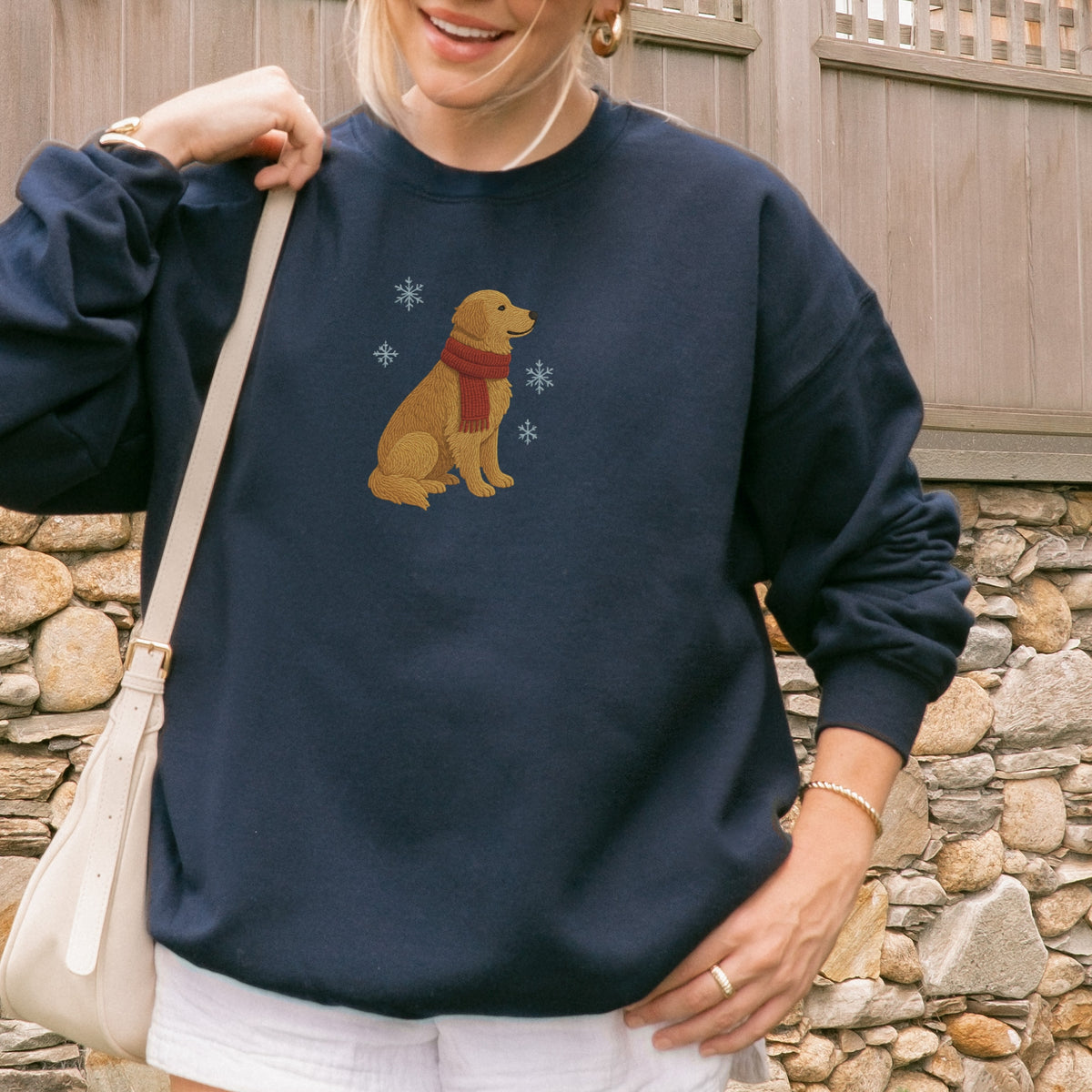 Person wearing a navy sweatshirt with a dog design, standing against a stone wall.