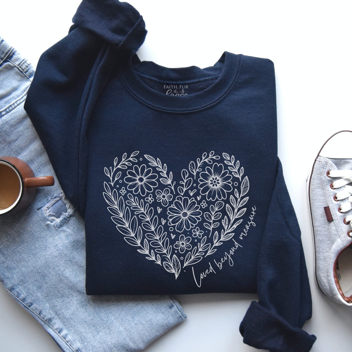 Navy blue sweatshirt with floral heart design on a white surface with jeans and a shoe.