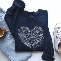 Navy blue sweatshirt with floral heart design on a white surface with jeans and a shoe.